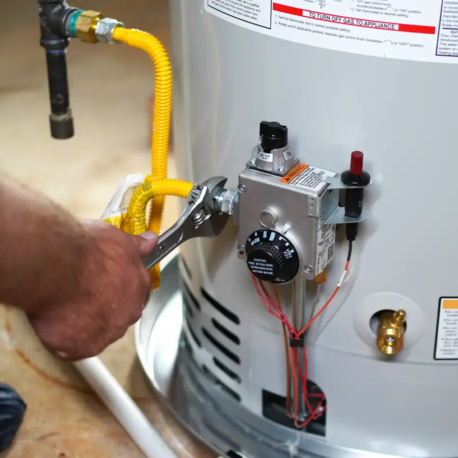 Close up of a gas line on a water heater with a plumber's hand holding a wrench