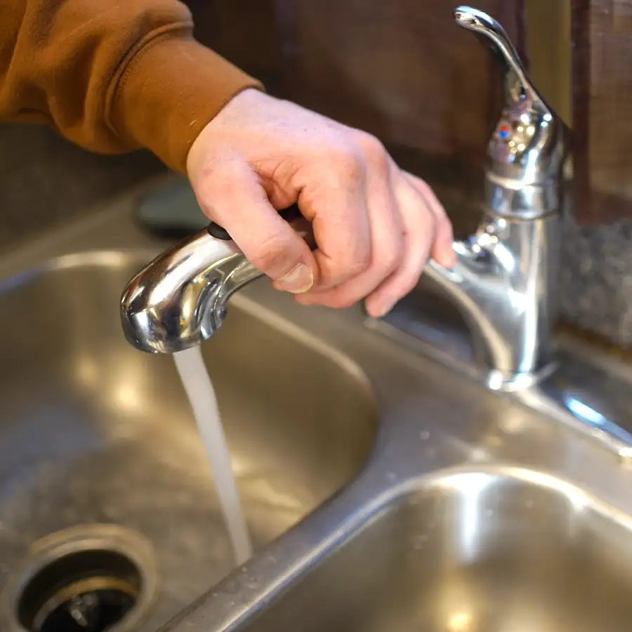 Close up of a hand resting on a sink's water faucet with the water running