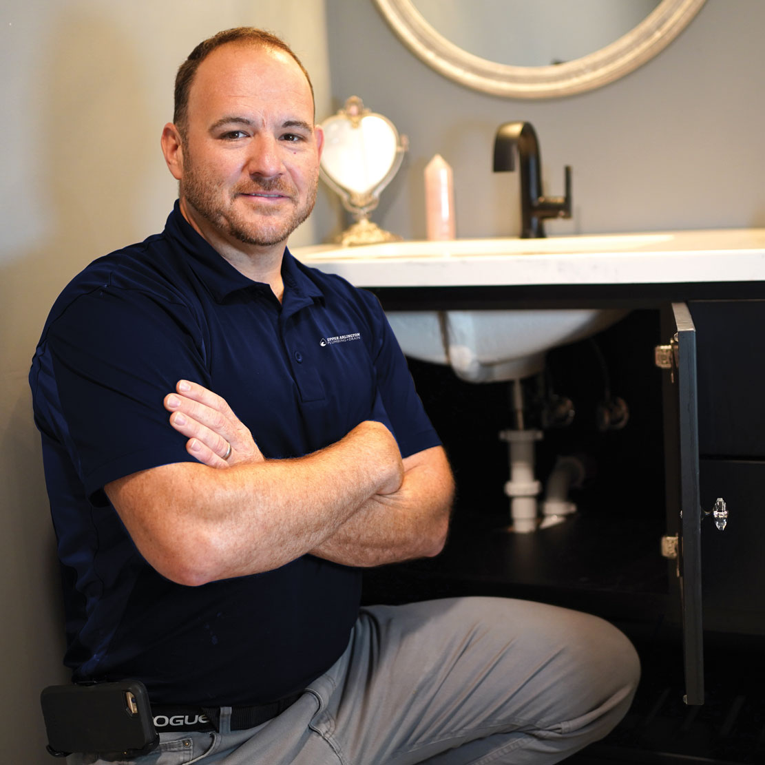 Plumber kneeling in a bathroom next to a sink