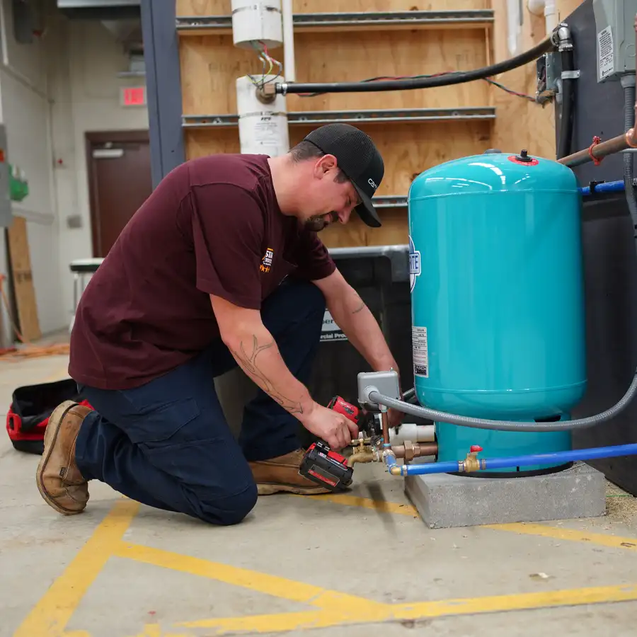 Plumbing with a drill kneeling next to a well pump