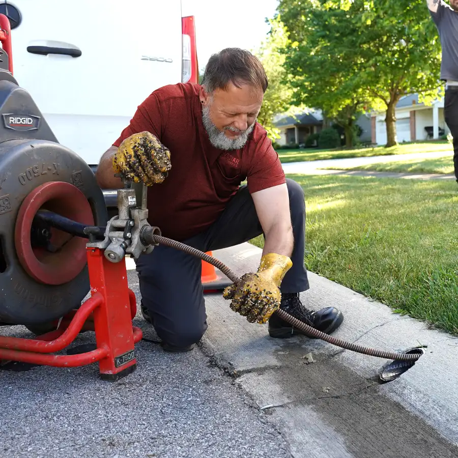 Plumber kneeling cleaning out a sewer with plumbing equipment